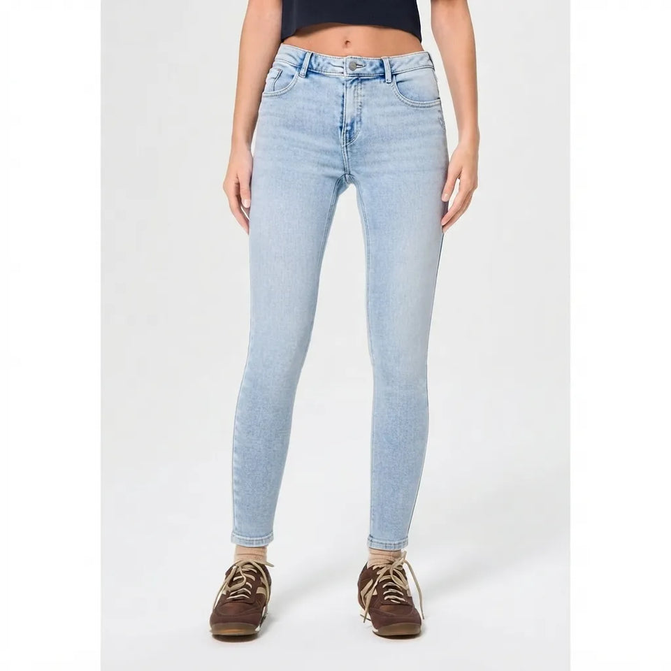 A model wearing light-wash blue skinny jeans, a black crop top, and brown lace-up sneakers, standing against a light gray studio background.