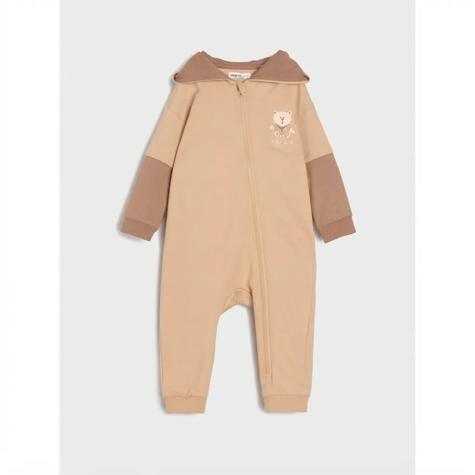 A baby hooded one-piece jumpsuit in beige and brown, featuring a small teddy bear graphic on the chest, displayed against a light gray background.