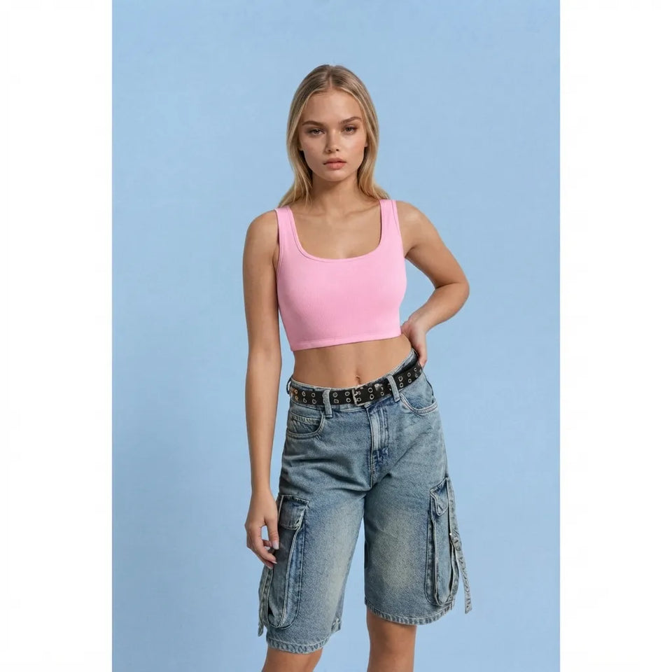 A model wearing a light pink scoop-neck crop top and light-wash blue denim cargo shorts with a black belt, standing against a solid light blue background.