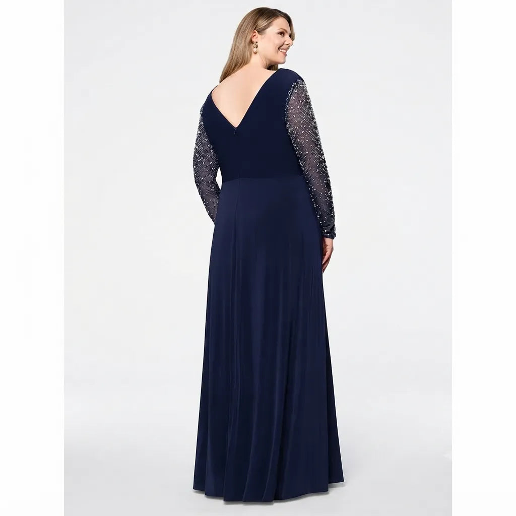 A woman modeling a navy blue floor-length gown from the back, featuring a deep V-neckline, a fitted waist, and long sheer beaded sleeves, set against a plain light gray studio background.