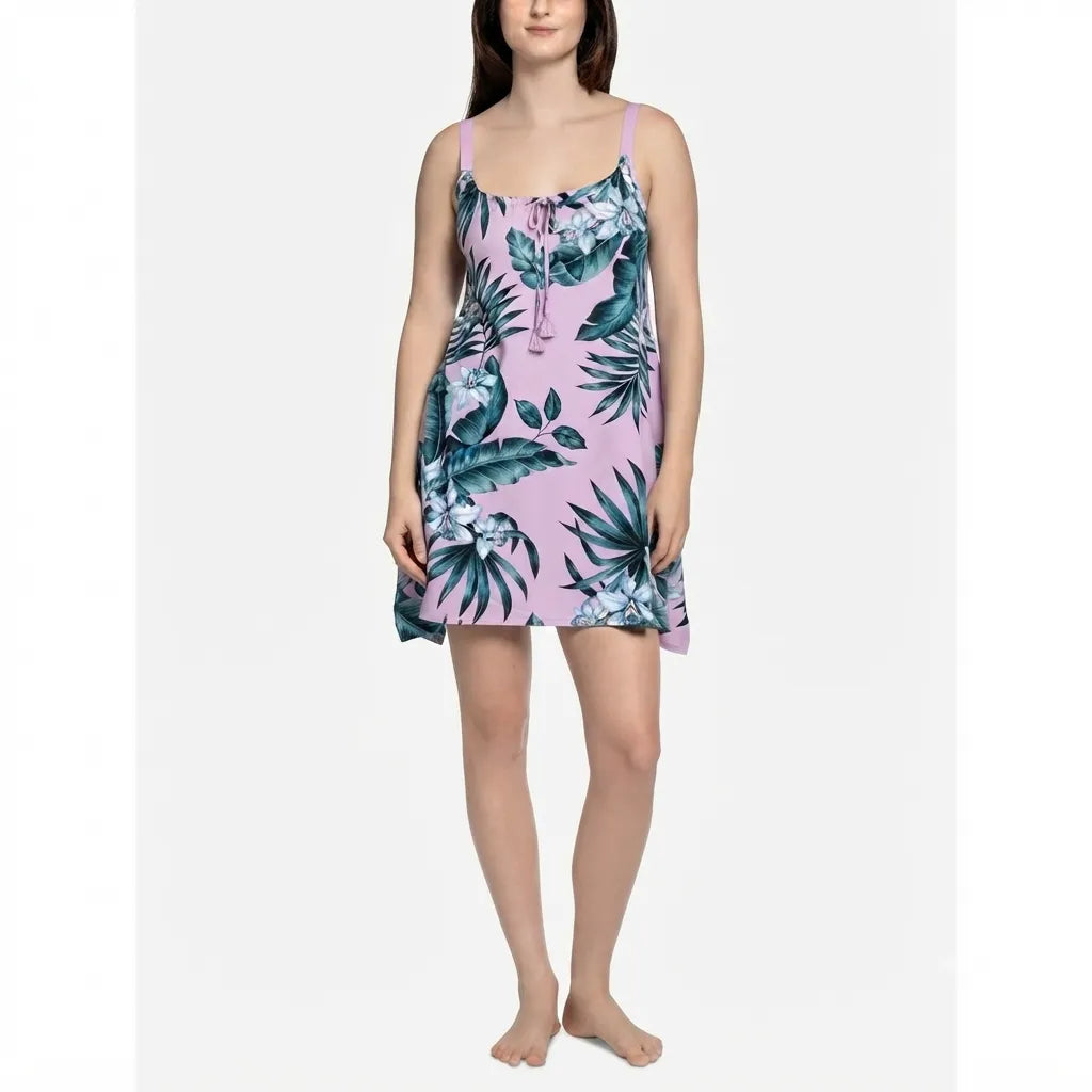 A woman modeling a short camisole nightgown with a tropical print on a light pink background, featuring green palm leaves and blue-green birds. The image is shot against a plain light gray background.