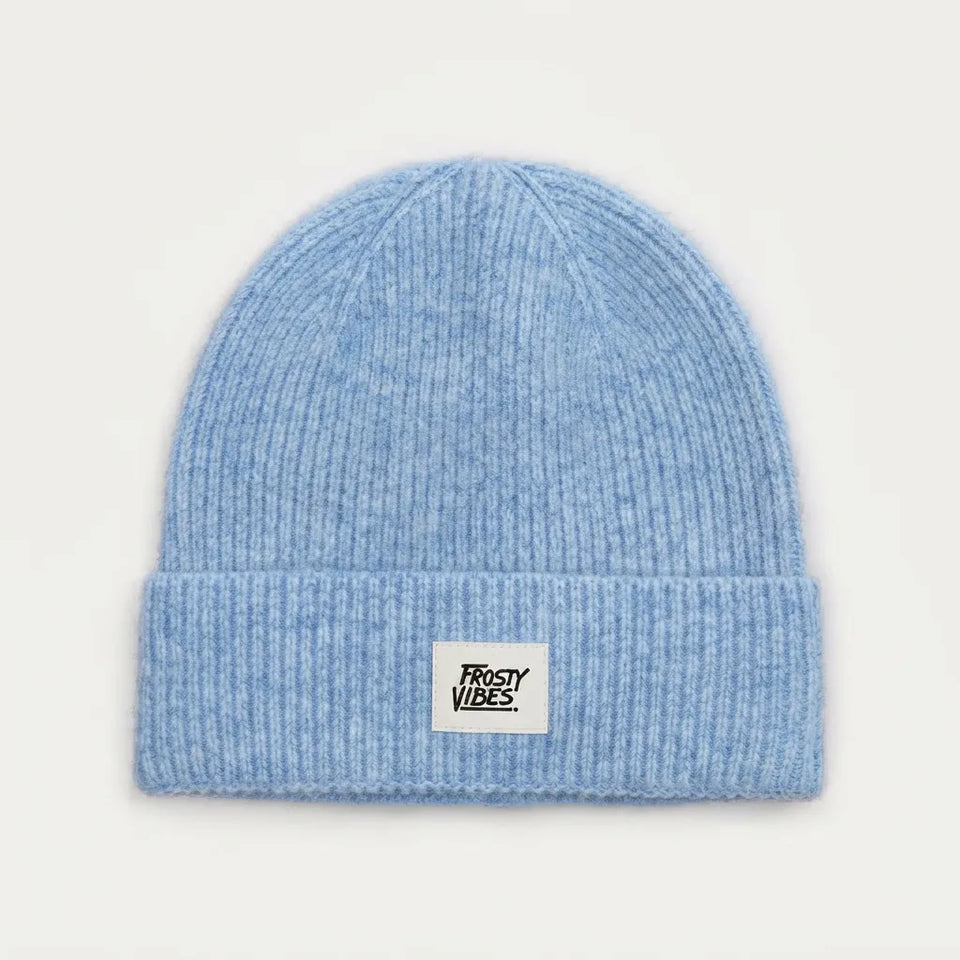 A light blue ribbed knit beanie hat with a folded cuff and a small white rectangular patch on the front that reads 'TRISTY VIBES'.