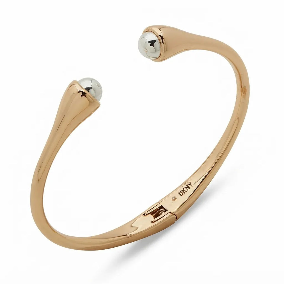 A polished rose gold cuff bracelet with a small faceted silver gemstone set in each end, shown on a clean white background. The brand name 'DKNY' is engraved inside the band.