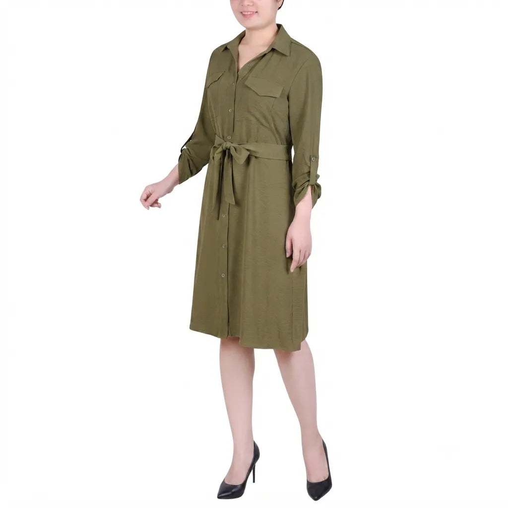 A woman modeling an olive green military-style shirt dress with a tie waist belt, button-down front, and three-quarter sleeves, paired with black high heels against a plain white background.