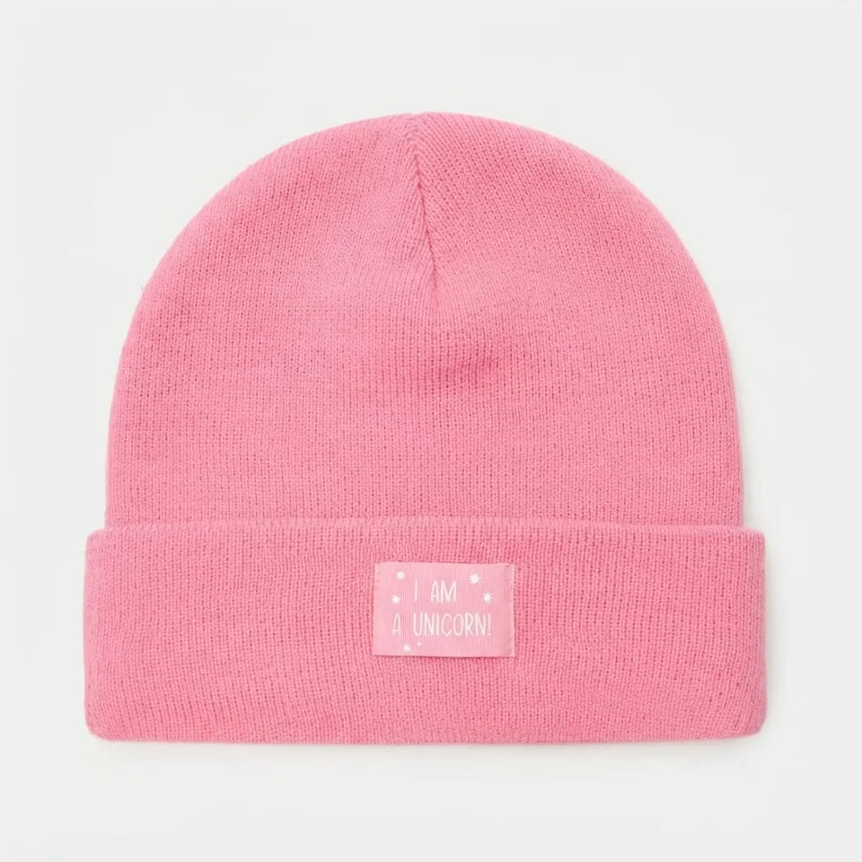 A pink knit beanie hat with a folded cuff, featuring a small rectangular patch on the front that reads 'I AM A UNICORN!' in white text with small white star details.