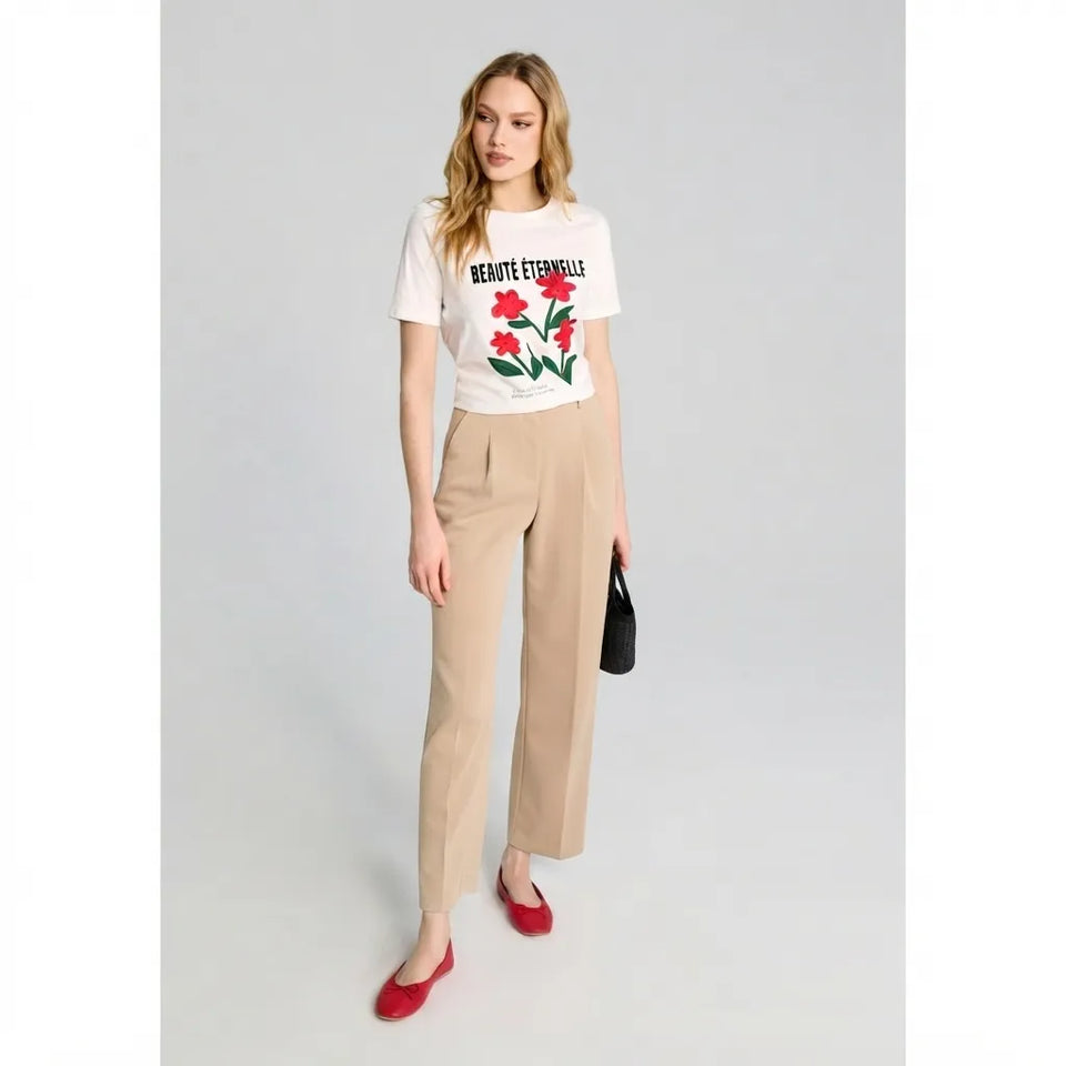 A woman modeling a white graphic T-shirt with red tulips and the text 'RENOUTE EVERYDAY', paired with beige wide-leg trousers and red flats, holding a small black handbag against a light gray studio background.