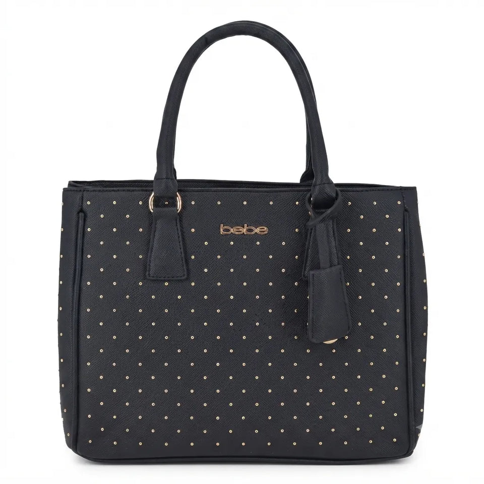 A black tote bag with a pattern of small gold studs and a gold-tone 'bebe' logo on the front, featuring dual top handles and a hanging leather tag, set against a plain white background.