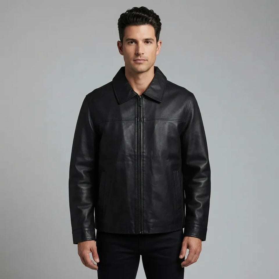 A man wearing a black leather jacket with a zippered front and collar, standing against a solid gray studio background.