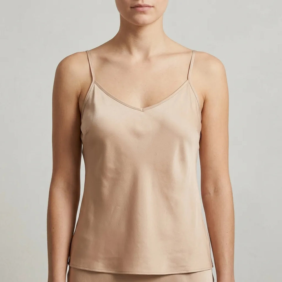 A woman wearing a light beige satin camisole top with thin spaghetti straps and a V-neckline, shown from the chin down against a neutral light gray background.