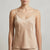 A woman wearing a light beige satin camisole top with thin spaghetti straps and a V-neckline, shown from the chin down against a neutral light gray background.