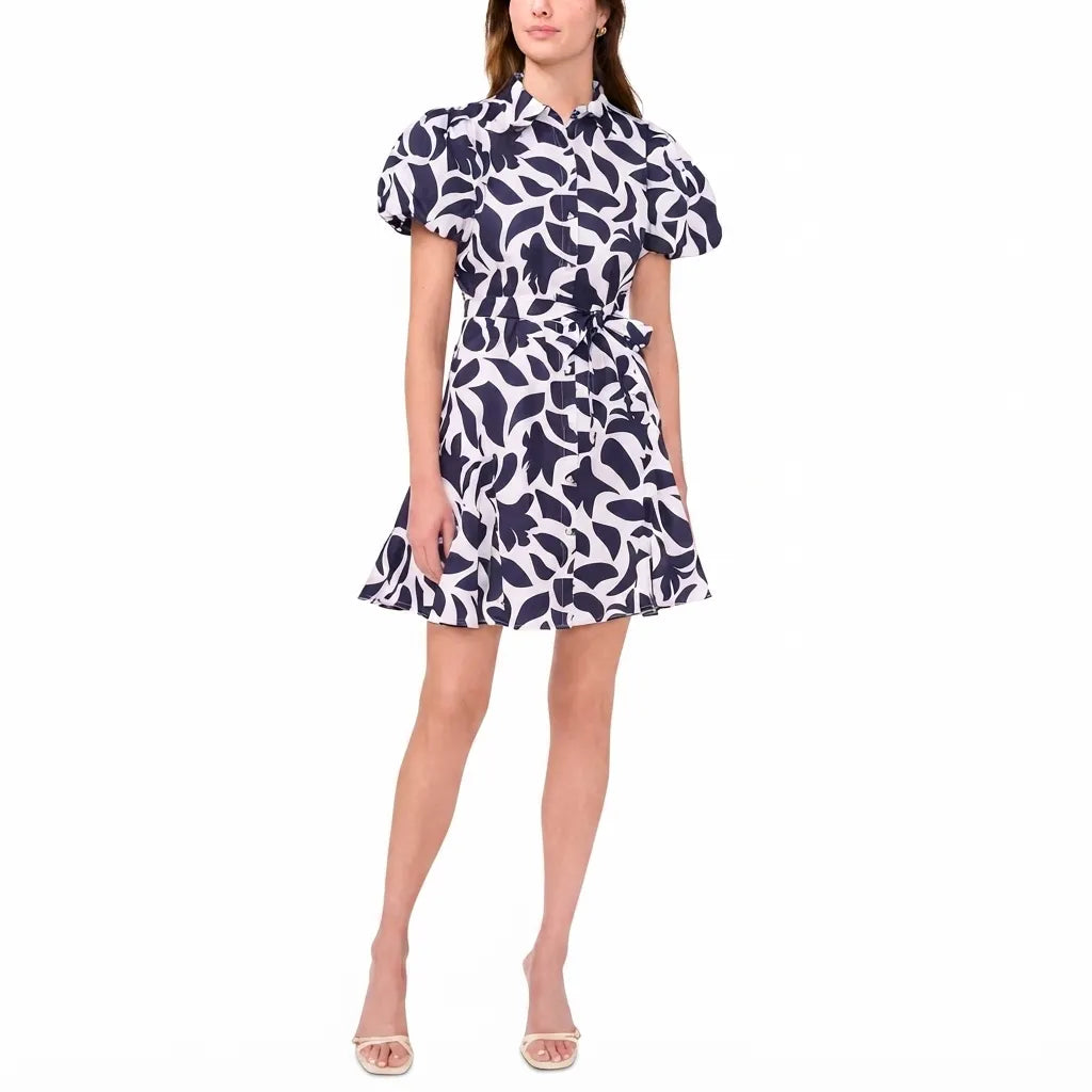A woman modeling a short puff-sleeve collared dress with a navy and white abstract floral pattern, shown against a plain white studio background.