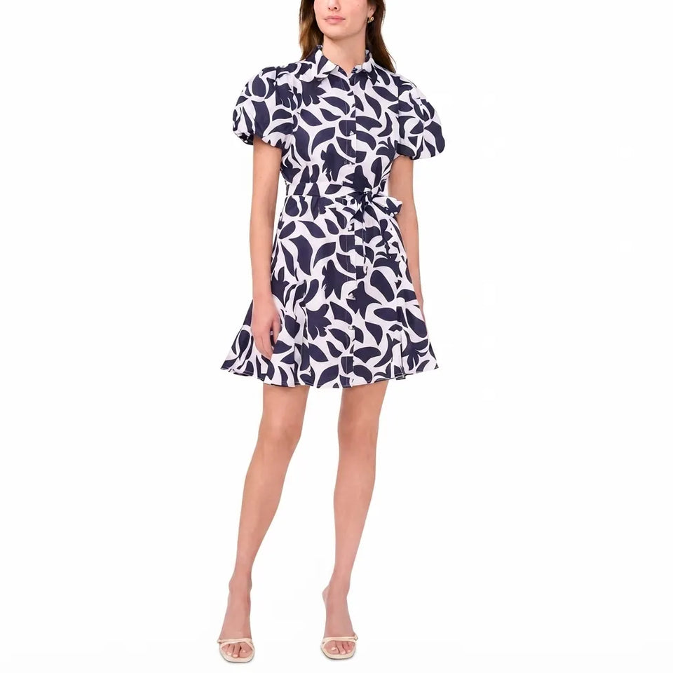 A woman modeling a short puff-sleeve collared dress with a navy and white abstract floral pattern, shown against a plain white studio background.