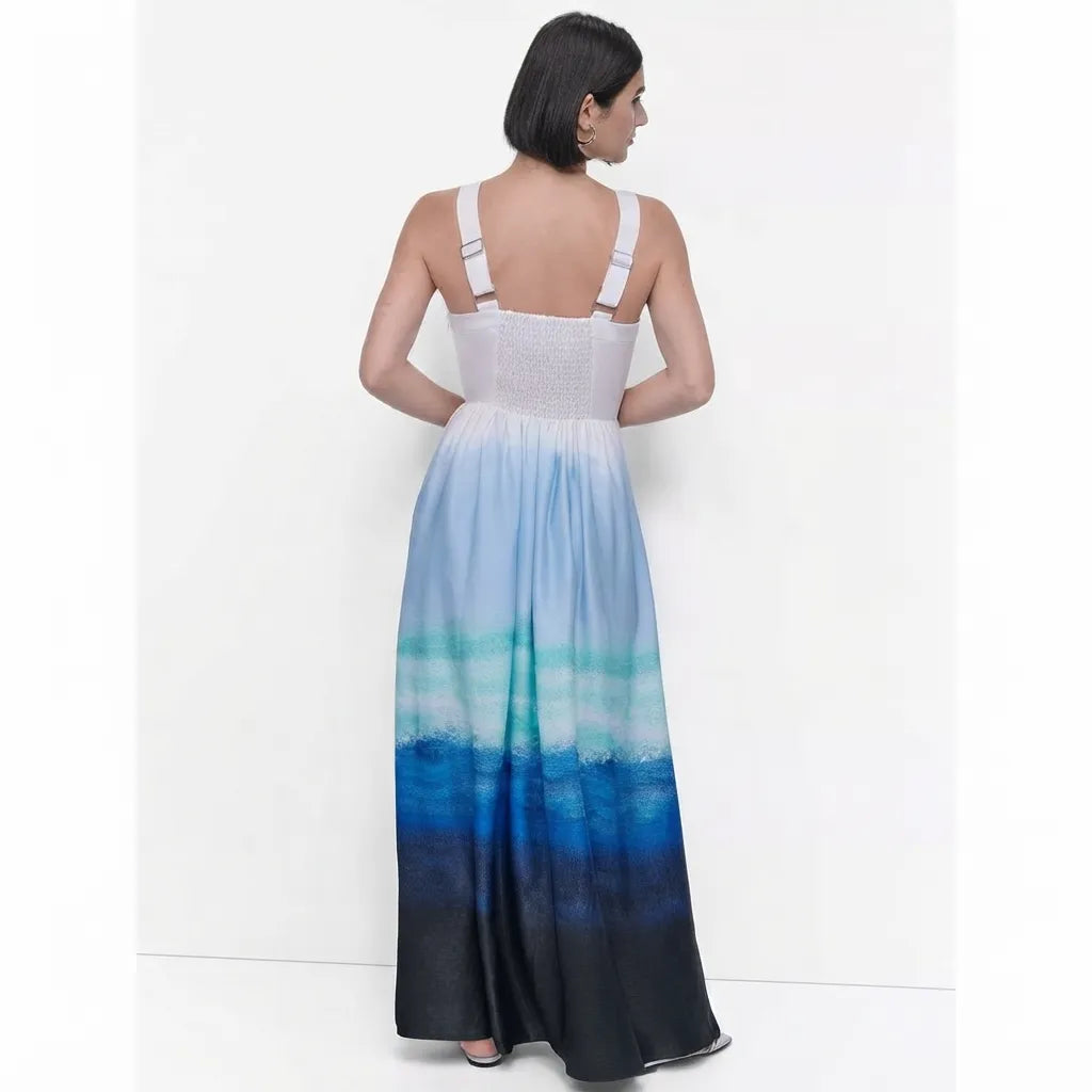 A woman viewed from the back wearing a sleeveless maxi dress with a white textured bodice and a flowing skirt that fades from light blue and teal into deep blue and black.