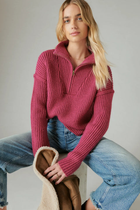 Woman wearing a pink ribbed sweater and blue jeans sitting on a white stool.