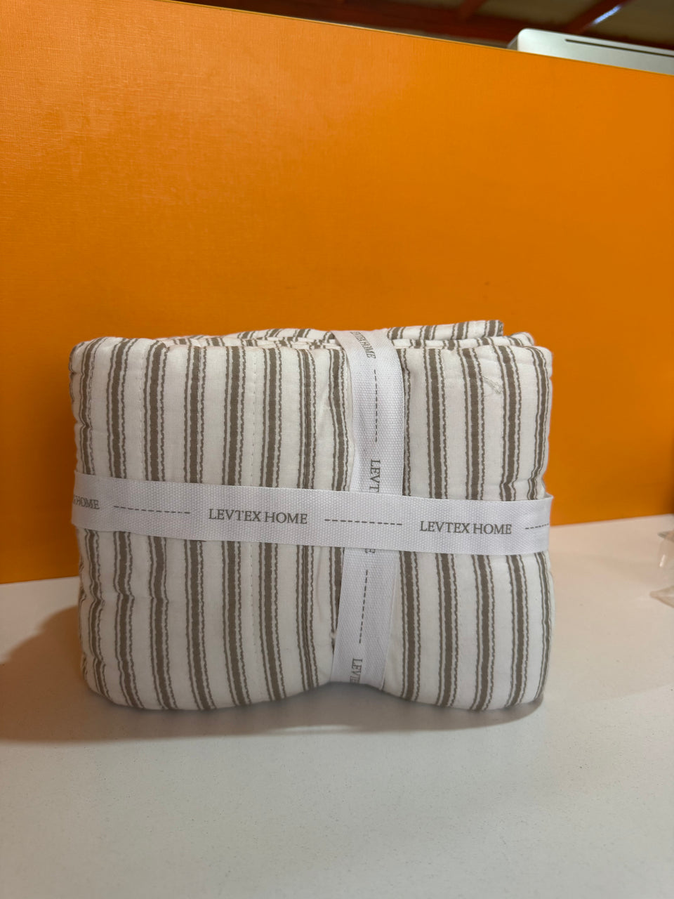 Folded fabric with 'LevTex Home' label against an orange background