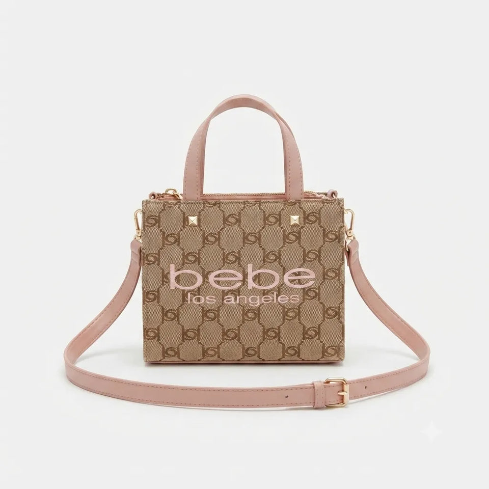 A beige and brown monogram handbag with pink handles and strap, featuring gold hardware and the text 'bebe los angeles' printed on the front, set against a light gray background.