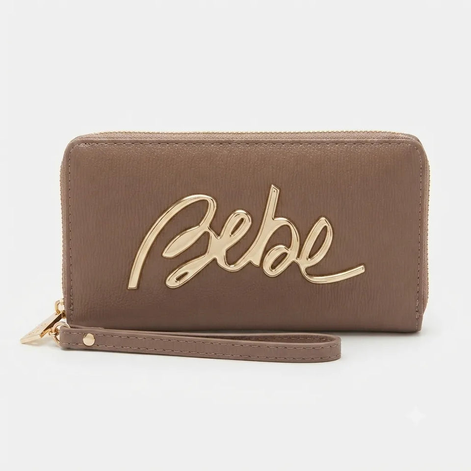 A brown leather zip-around wallet with a wristlet strap and a large gold metallic 'Bebe' script logo on the front, set against a plain light gray background.