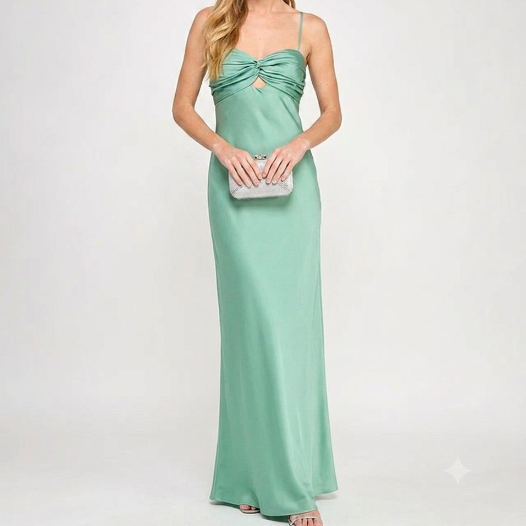 A woman modeling a floor-length mint green satin gown with spaghetti straps, a sweetheart neckline, and a gathered sweetheart bodice. She is holding a small silver clutch against a plain light gray studio background.