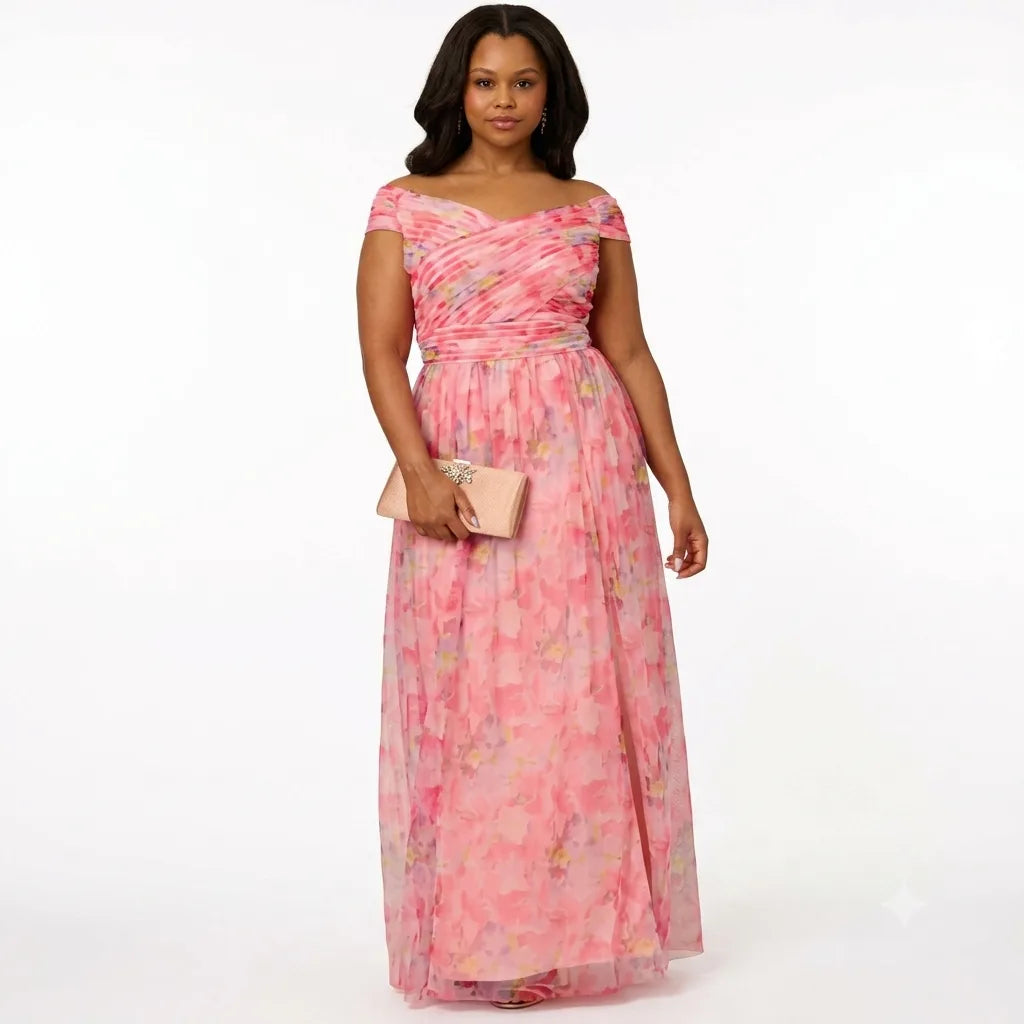A woman modeling a pink off-the-shoulder maxi dress with a floral watercolor print, holding a small beige clutch against a plain white studio background.