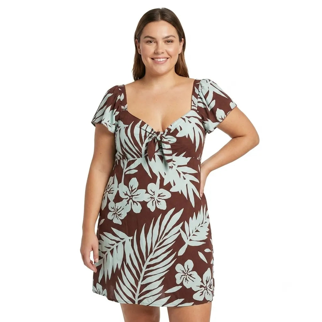 A woman modeling a brown and light blue tropical floral print mini dress with short flutter sleeves and a tie-front neckline, photographed against a plain white background.