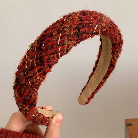 Red knitted headband held by a hand against a plain background