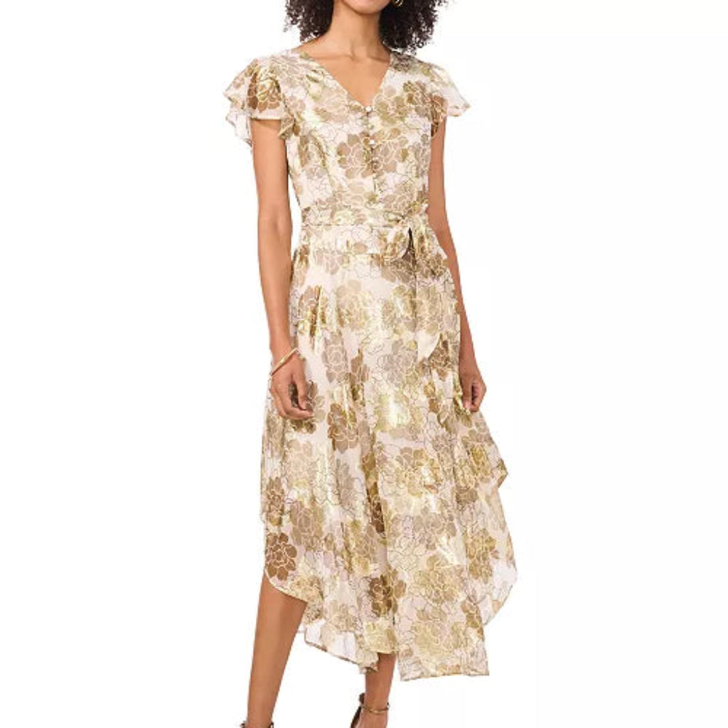 A woman models a short-sleeved midi dress with a ruffled V-neckline, a matching waist tie, and a gold floral pattern on a cream background, paired with gold high-heeled sandals against a plain white background.