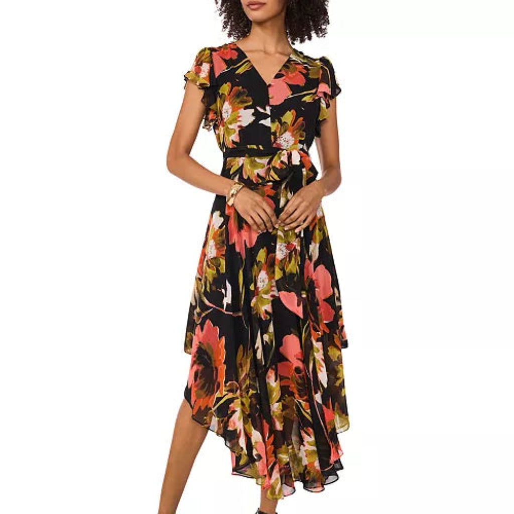 A woman models a black midi wrap dress with a vibrant floral print in pink, orange, and yellow, paired with black strappy high-heeled sandals against a plain white background.