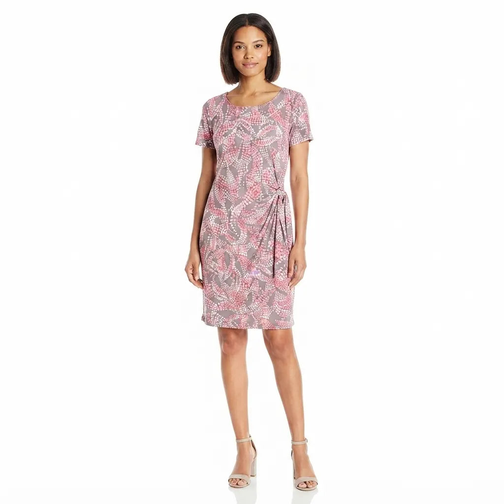 A woman modeling a short-sleeve knee-length dress with a pink, gray, and white tropical leaf print, standing against a plain white background.
