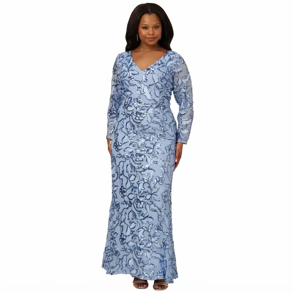 A woman modeling a light blue long-sleeve maxi dress with a dark blue floral lace overlay, standing against a plain white background.