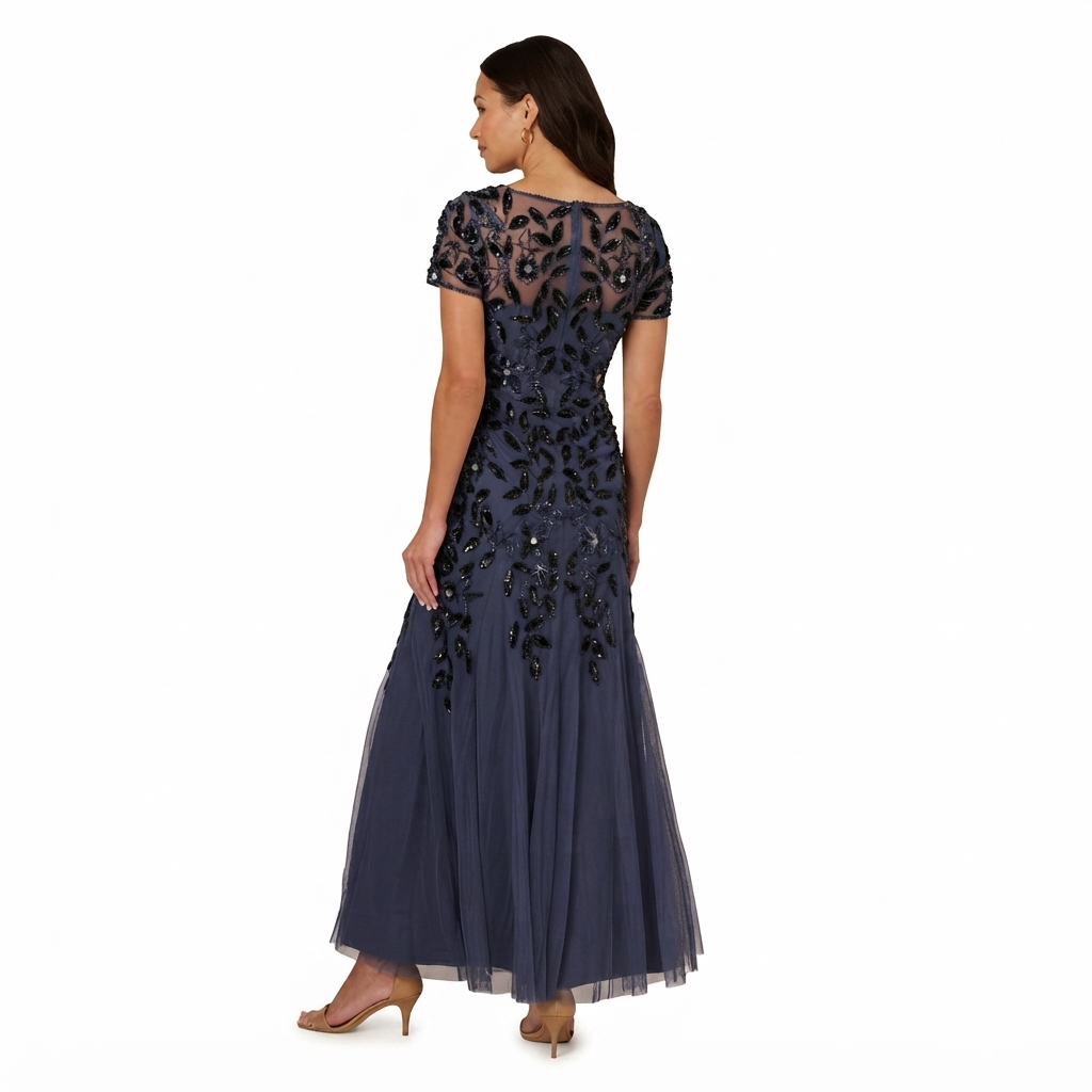 A woman modeling a navy blue floor-length evening gown from the back, featuring sheer lace short sleeves, a heavily embellished beaded back bodice, and a flowing tulle skirt, set against a plain white background.