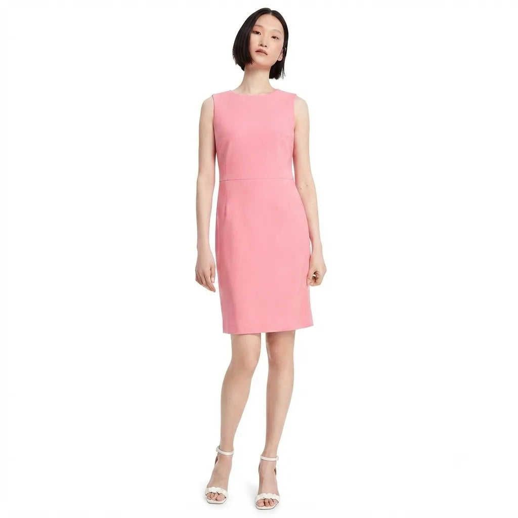 A woman modeling a sleeveless pink knee-length dress with a structured, slightly fitted silhouette and a straight neckline, paired with white heeled sandals, against a plain white background.
