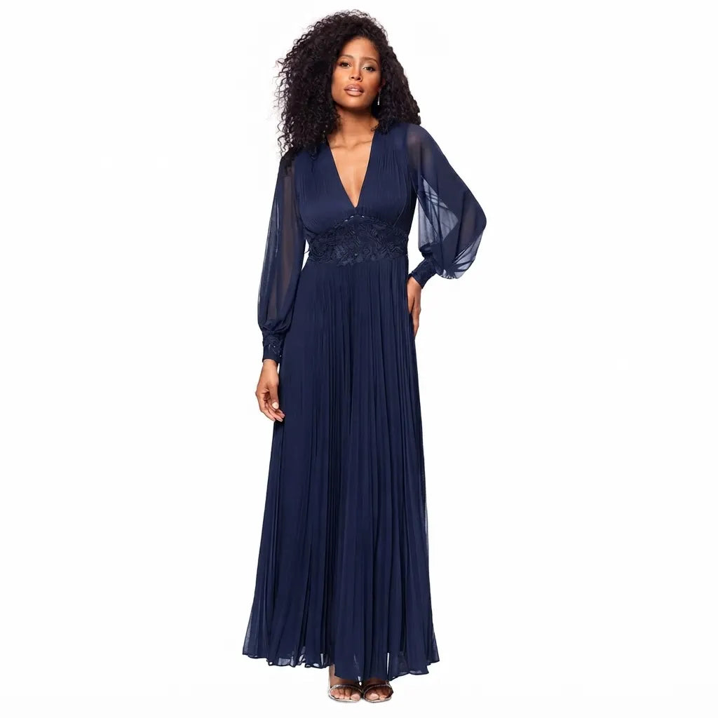 A woman modeling a navy blue maxi dress with a deep V-neckline, sheer long balloon sleeves, a lace-embroidered waist, and a flowing pleated skirt, set against a plain white background.