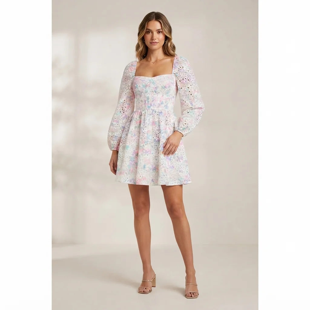 A woman modeling a short white puff-sleeve dress with a pastel multicolor floral print, photographed against a warm beige studio background.