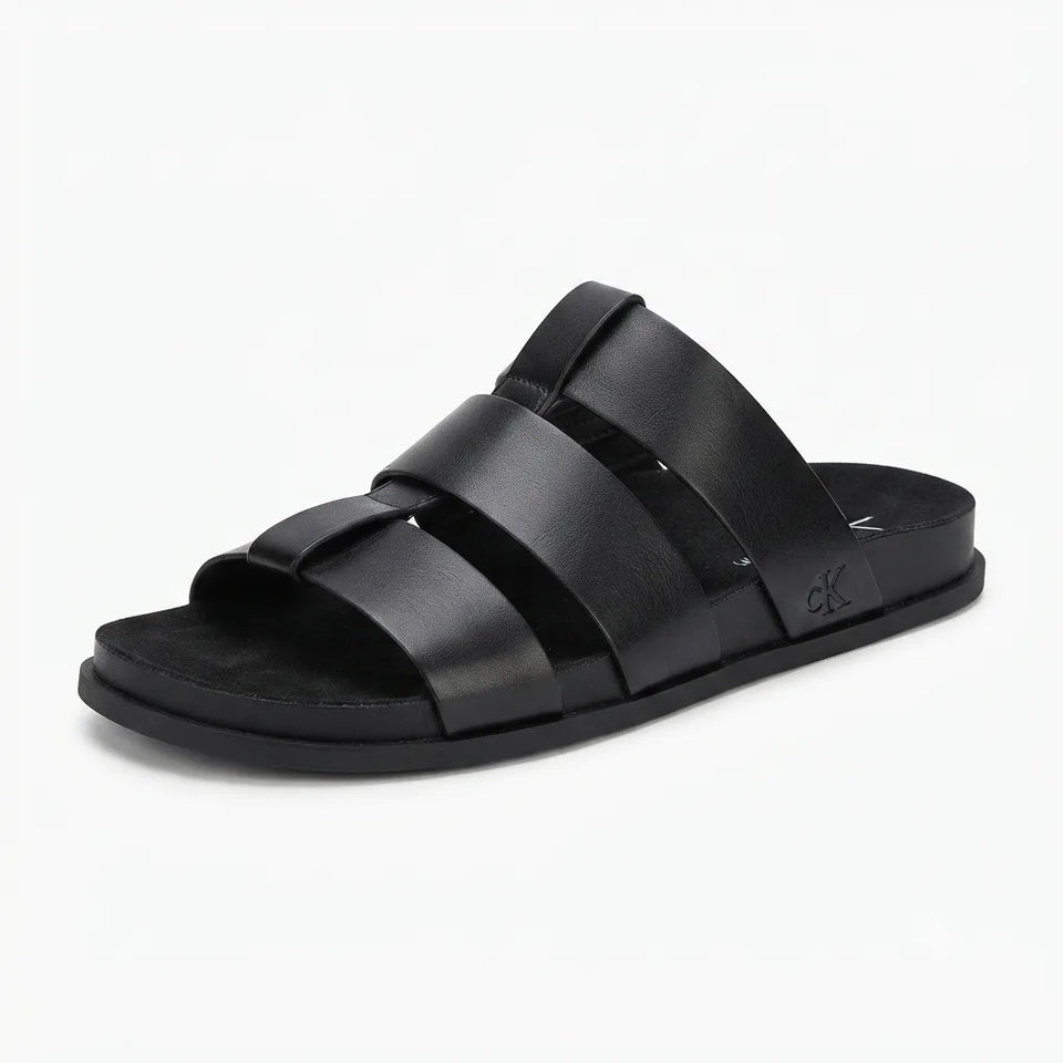 A single black leather slide sandal with three wide horizontal straps and a low black sole, featuring a small embossed CK logo on the heel, shown against a plain white background.