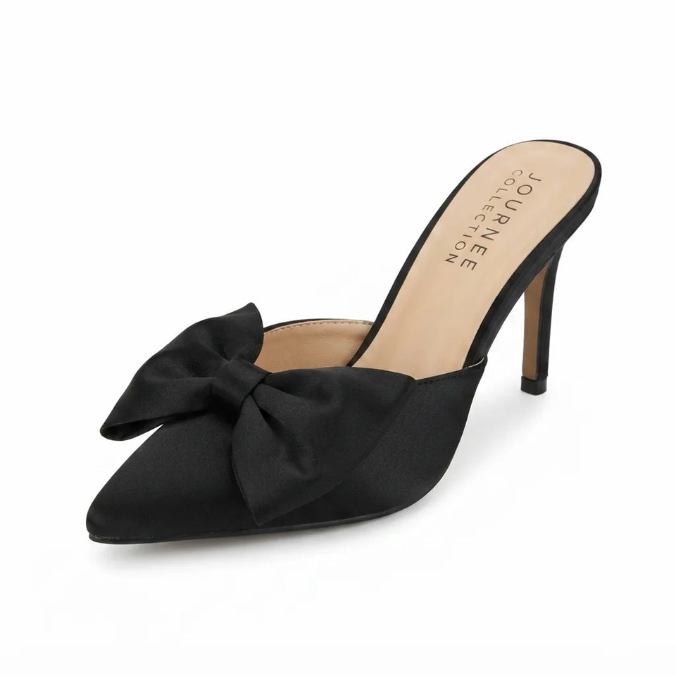 A single black satin pointed-toe mule heel with a large bow on the toe, shown on a clean white background. The insole displays the brand name 'JOURNEE collection'.