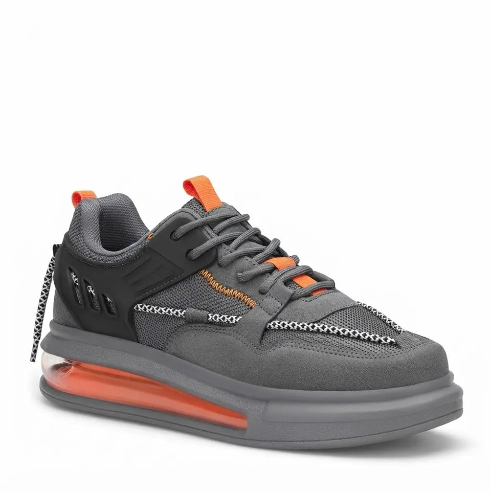 A gray low-top sneaker with orange accents, featuring a chunky translucent orange and gray sole, gray laces, and decorative chain-like overlays on the side, shown against a plain white background.
