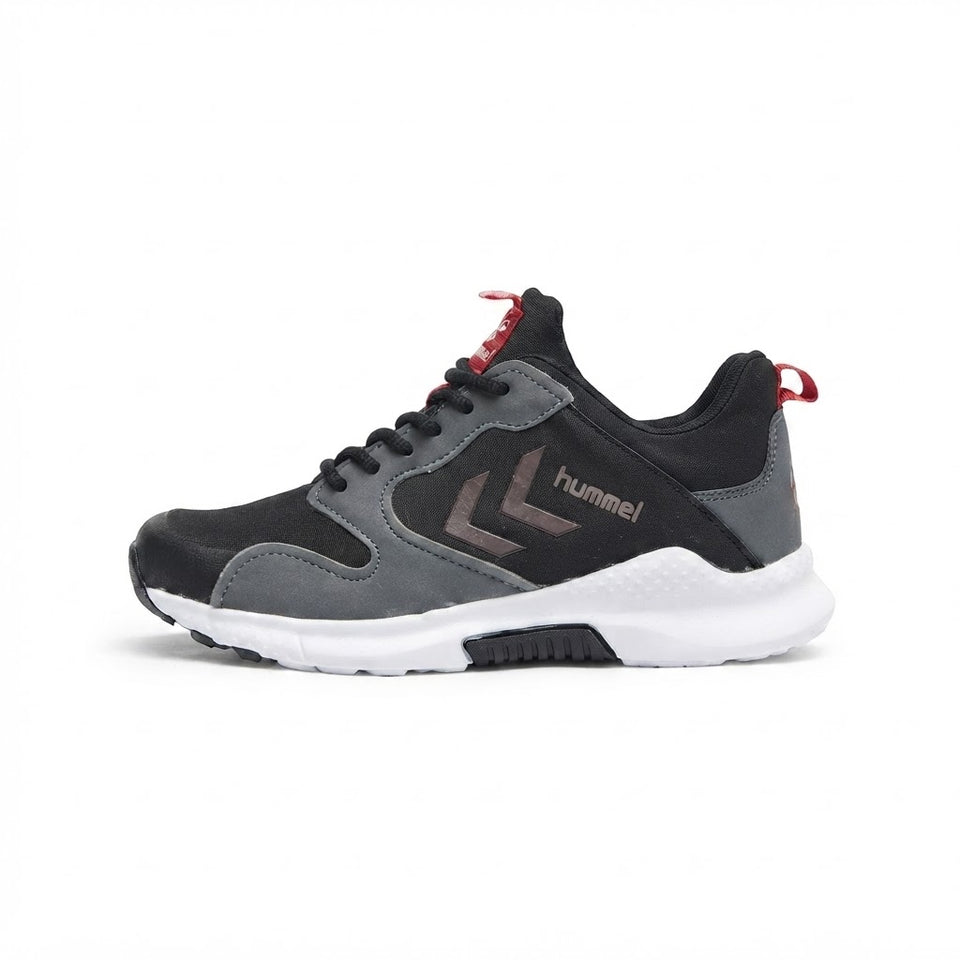 A low-top athletic sneaker in black and gray suede and mesh, featuring a white midsole, a brown chevron logo with the 'hummel' brand name, and red accents on the tongue and heel pull tab, shown against a plain white background.