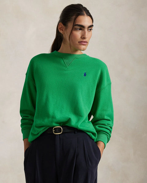 Person wearing a green sweater with a logo on a beige background