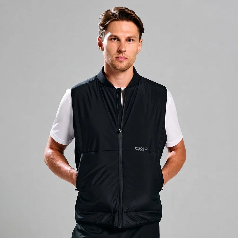 A man wearing a black sleeveless zip-front vest over a white short-sleeve shirt, photographed against a plain light gray studio background. The vest has a small visible SANC logo on the left chest.