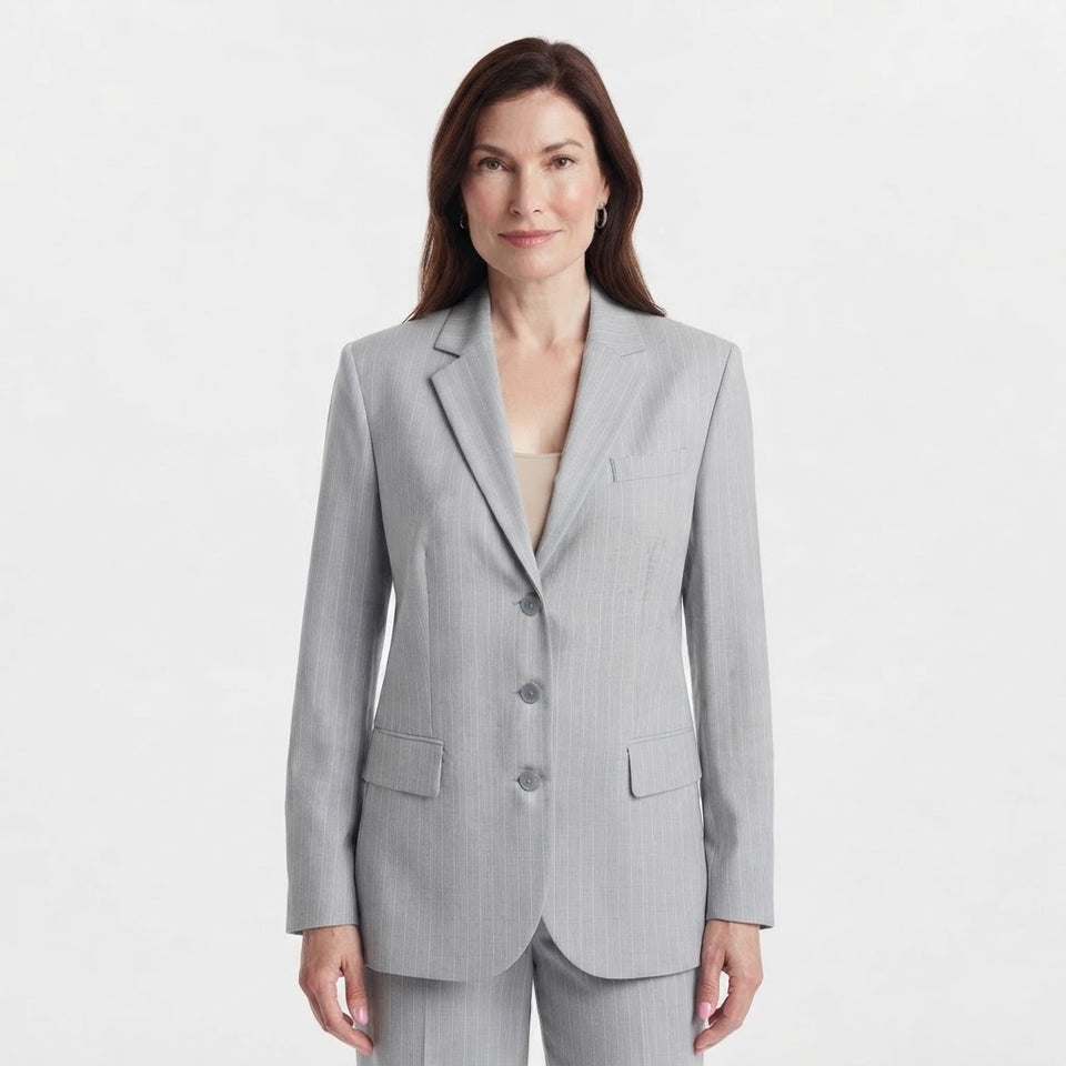 A woman modeling a light gray pinstripe blazer with matching trousers against a clean white studio background.