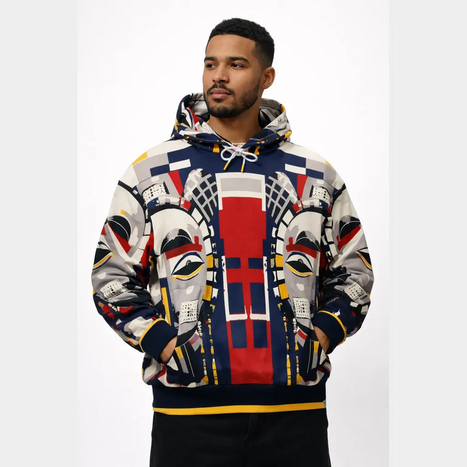 A man wearing a pullover hoodie with a complex, colorful graphic print featuring stylized faces, geometric shapes, and bold blocks of red, navy, yellow, white, and black, set against a plain light gray background.