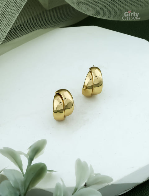 Gold hoop earrings on a white surface with greenery in the background, branded 'Girly Grove'.
