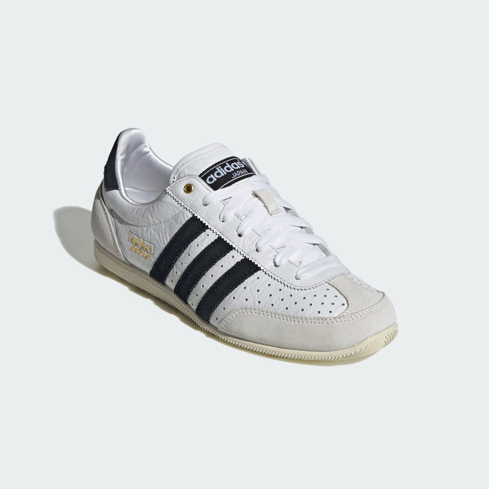 White Adidas sneaker with black stripes on a light gray background