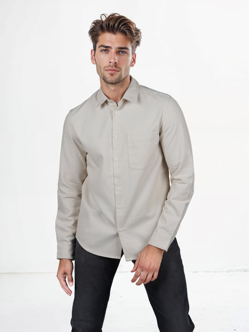 Man wearing a beige button-up shirt and black pants on a white background