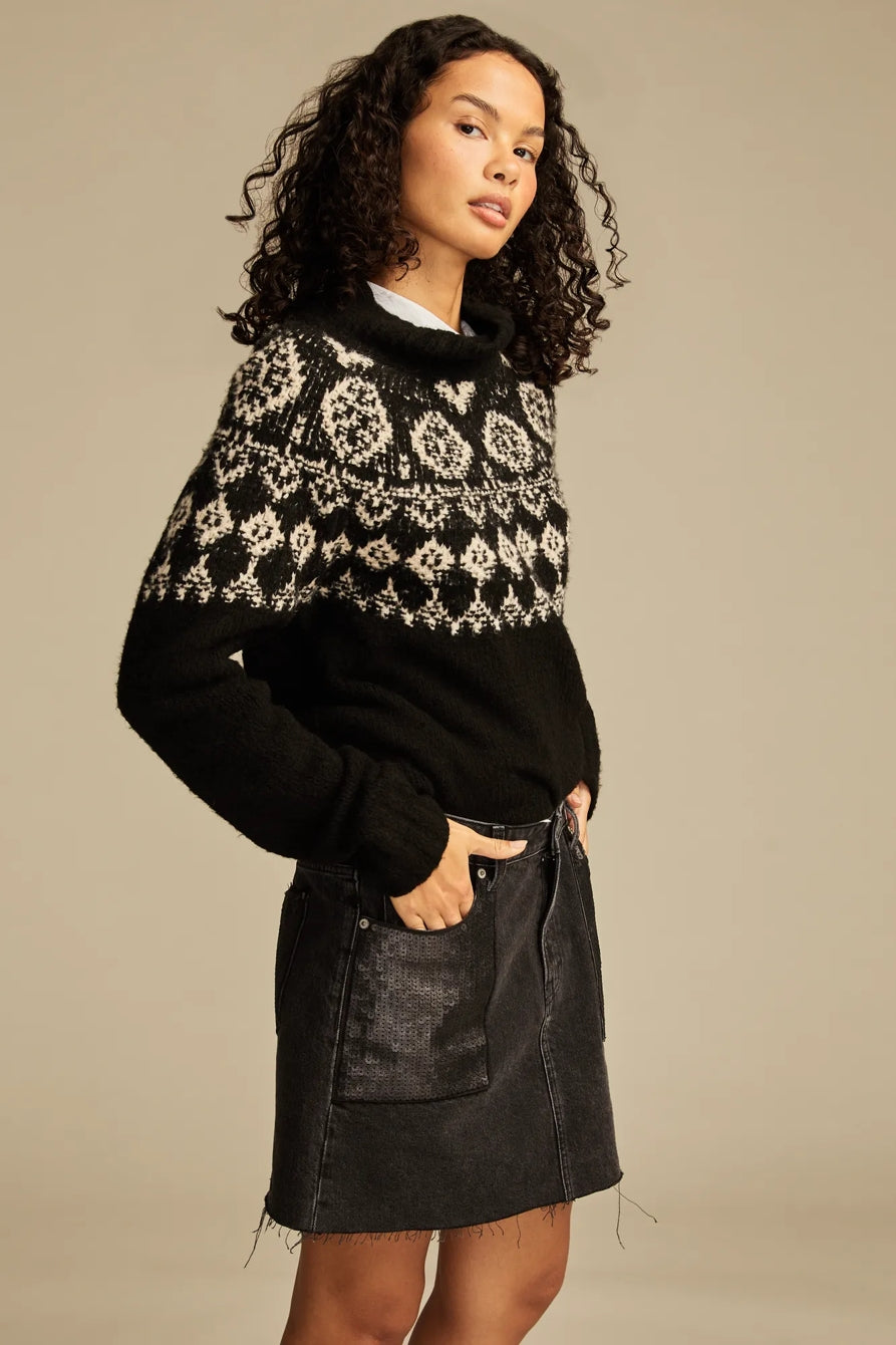 Woman wearing a black and white patterned sweater with a plain background