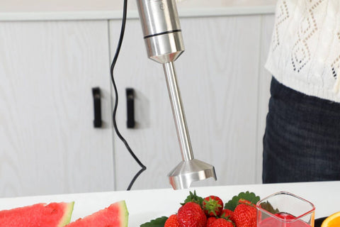 Handheld blender being used to blend fruits on a kitchen counter.