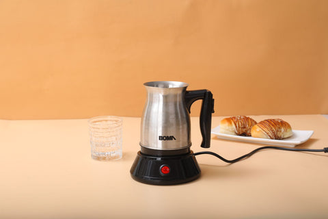 Small electric kettle on a table with a glass and pastries in the background