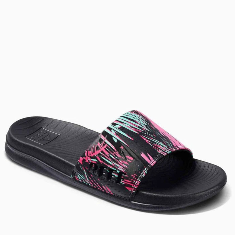 A single slide sandal with a black sole and strap, featuring a vibrant abstract pattern in hot pink and light blue on the upper strap, shown against a plain white background.