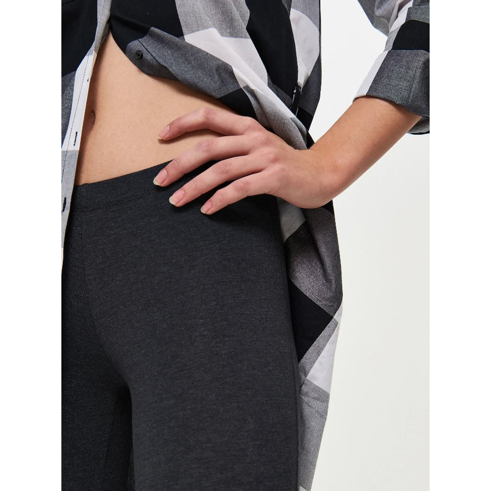 Close-up of a model wearing dark charcoal gray heathered leggings and an open black, white, and gray plaid shirt, with one hand resting on the hip.