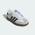 A single Adidas Samba sneaker in white, gray, and black, shown from a three-quarters angle on a light gray background.